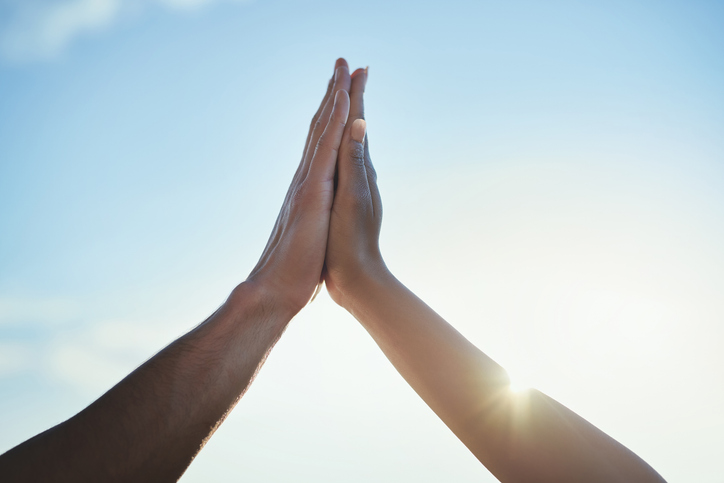 Two hands giving a high five against a bright blue sky, celebrating Nadia and Todd as March Winners with sunlight shining in the background.