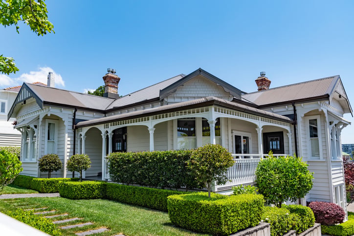 A charming, light-colored Victorian-style house with a wraparound porch, intricate trim, manicured hedges, and green lawn under a clear blue sky—an inviting haven amid evolving 2026 mortgage trends.