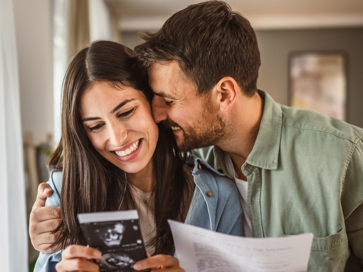 Smiling couple looking at a baby ultrasound scan together at home — illustrating a qualifying life event that may allow you to increase your New Zealand insurance cover without new medical underwriting.